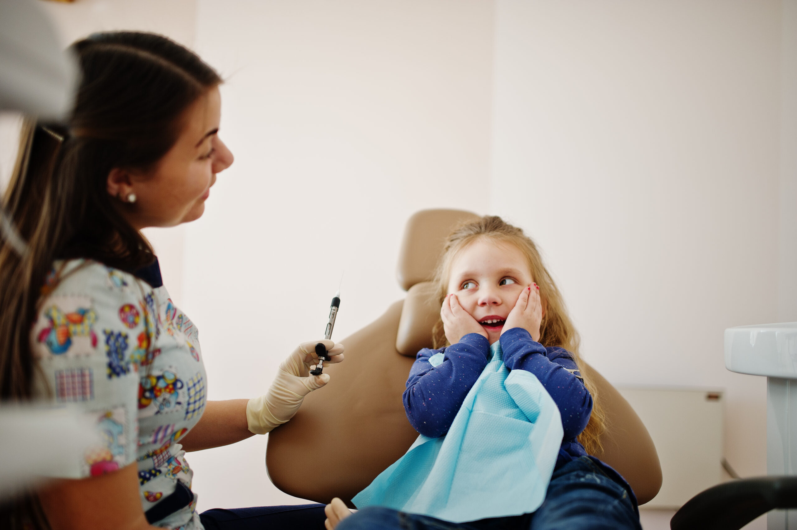 Criança sentada na cadeira do consultório odontológico, conversando com a dentista sobre a extração do dente de leite.