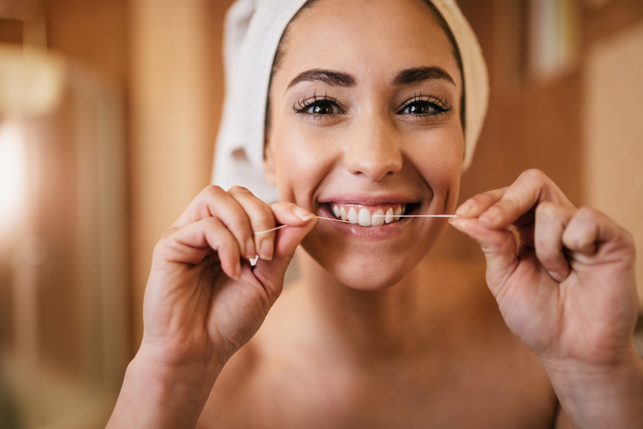 Mulher jovem e sorridente, com uma toalha na cabeça, mostrando como usar fio dental.