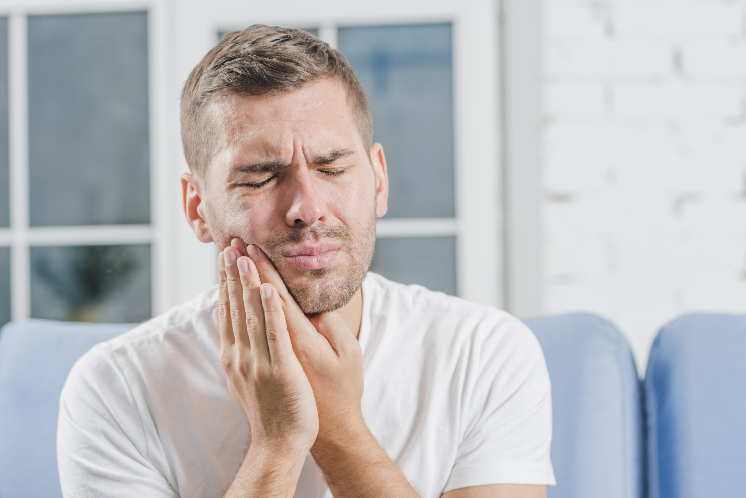 Homem jovem, branco, em sua casa, sofrendo com dor nos dentes.