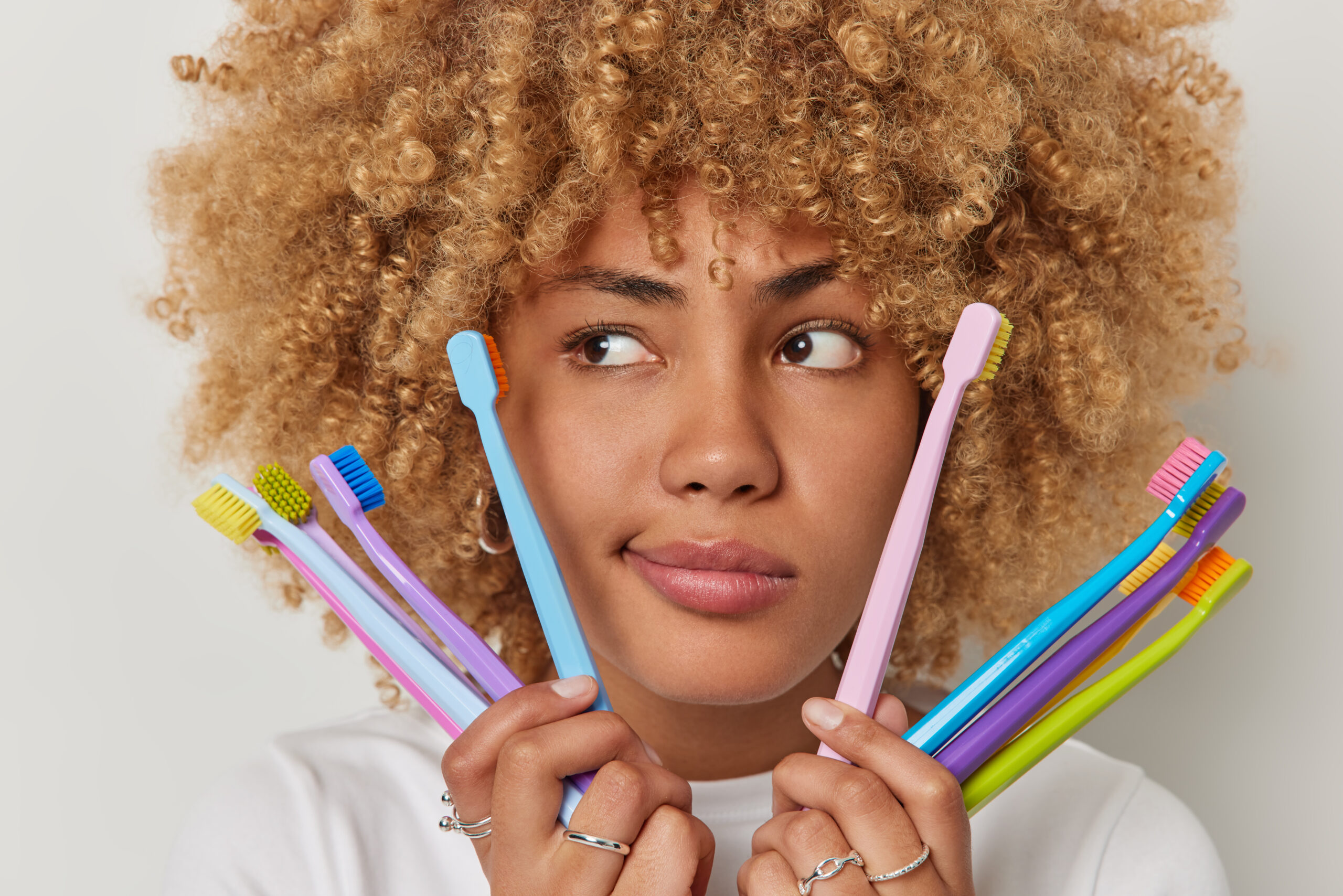 Mulher negra e jovem segurando variados tipos de escovas de dentes.